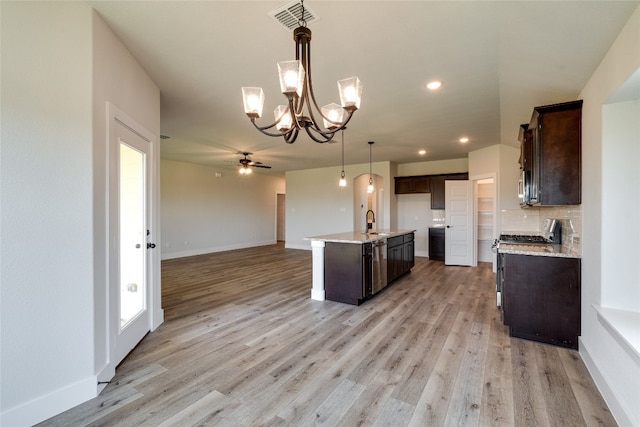 kitchen with hanging light fixtures, ceiling fan with notable chandelier, a kitchen island with sink, light hardwood / wood-style floors, and stainless steel appliances