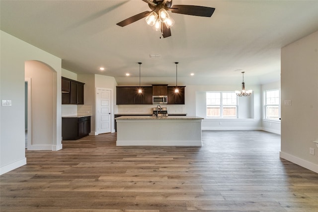 kitchen featuring an island with sink, backsplash, ceiling fan with notable chandelier, and pendant lighting