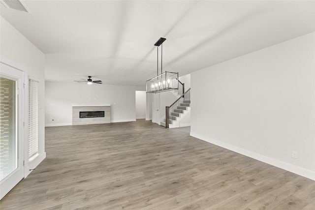 unfurnished living room with a tiled fireplace, ceiling fan with notable chandelier, and light hardwood / wood-style flooring