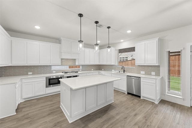 kitchen featuring tasteful backsplash, stainless steel appliances, light hardwood / wood-style floors, decorative light fixtures, and white cabinets