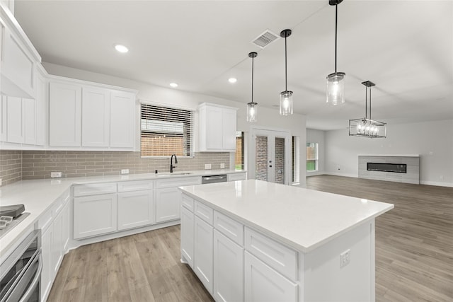 kitchen with light hardwood / wood-style floors, a center island, decorative light fixtures, appliances with stainless steel finishes, and sink