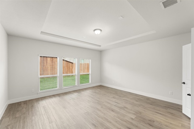 unfurnished room with light wood-type flooring and a raised ceiling