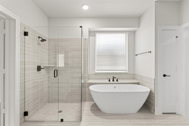 bathroom with tile walls, shower with separate bathtub, and tile floors