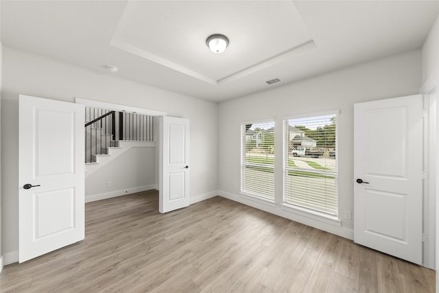 unfurnished room with a raised ceiling and light wood-type flooring