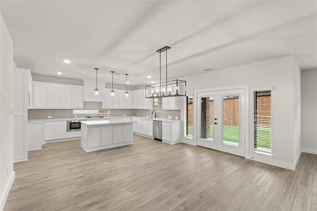 kitchen featuring appliances with stainless steel finishes, light wood-type flooring, white cabinets, a center island, and pendant lighting