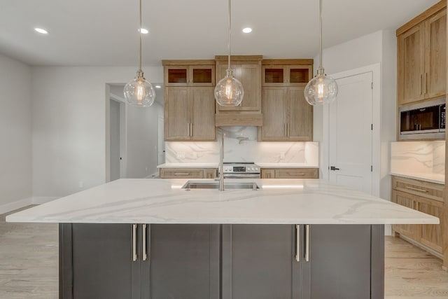 kitchen with decorative backsplash, stainless steel microwave, light hardwood / wood-style flooring, and a kitchen island with sink