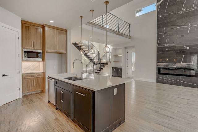 kitchen featuring stainless steel appliances, sink, decorative light fixtures, light wood-type flooring, and an island with sink