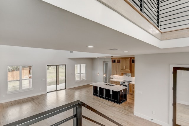 kitchen with sink, light hardwood / wood-style floors, a high ceiling, an island with sink, and stainless steel range with electric stovetop