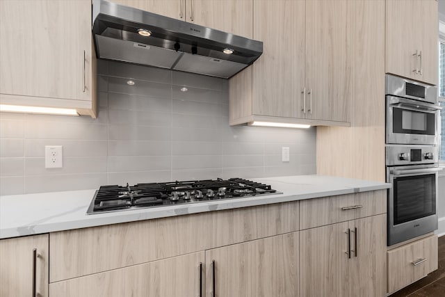 kitchen with stainless steel appliances, light stone counters, ventilation hood, backsplash, and light brown cabinetry