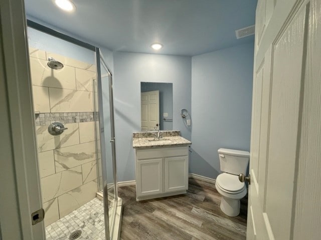 bathroom with toilet, tiled shower, vanity, and hardwood / wood-style flooring