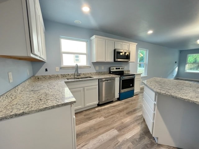 kitchen featuring sink, a healthy amount of sunlight, white cabinets, appliances with stainless steel finishes, and light hardwood / wood-style floors