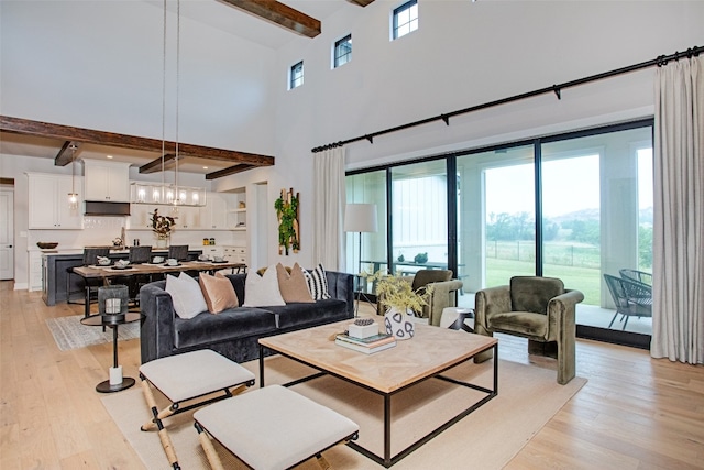 living room featuring beamed ceiling, a high ceiling, light hardwood / wood-style flooring, and an inviting chandelier