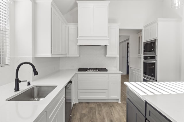 kitchen with appliances with stainless steel finishes, sink, decorative backsplash, white cabinetry, and hardwood / wood-style flooring