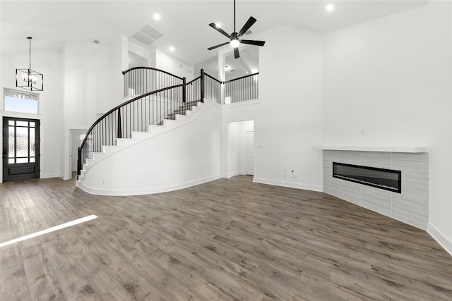 unfurnished living room with a fireplace, ceiling fan with notable chandelier, hardwood / wood-style flooring, and high vaulted ceiling