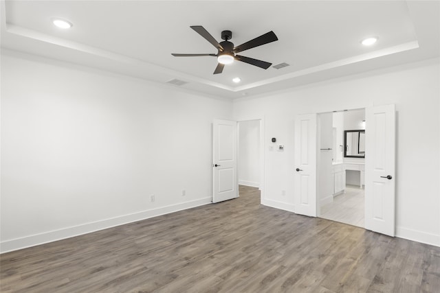 unfurnished bedroom with connected bathroom, a raised ceiling, hardwood / wood-style floors, and ceiling fan