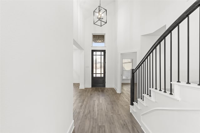 entrance foyer with an inviting chandelier, wood-type flooring, and a towering ceiling