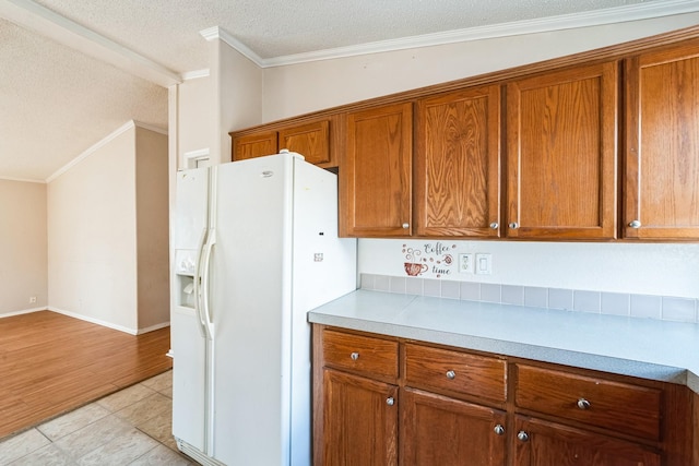 kitchen featuring crown molding, white refrigerator with ice dispenser, light tile patterned floors, and a textured ceiling