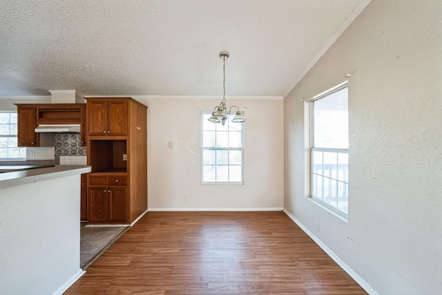 kitchen with dark hardwood / wood-style floors, pendant lighting, a wealth of natural light, a notable chandelier, and crown molding