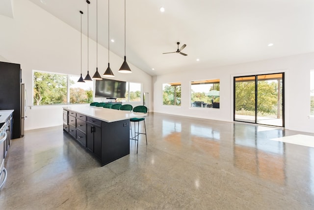 kitchen with concrete floors, a kitchen island, ceiling fan, a kitchen breakfast bar, and decorative light fixtures