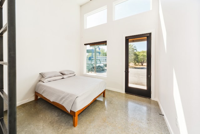 bedroom featuring multiple windows, concrete flooring, access to exterior, and a high ceiling