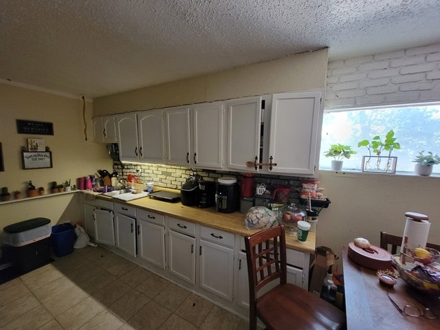 kitchen with light tile floors, white cabinetry, a textured ceiling, and backsplash