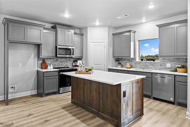 kitchen with sink, gray cabinetry, a center island, appliances with stainless steel finishes, and light hardwood / wood-style floors