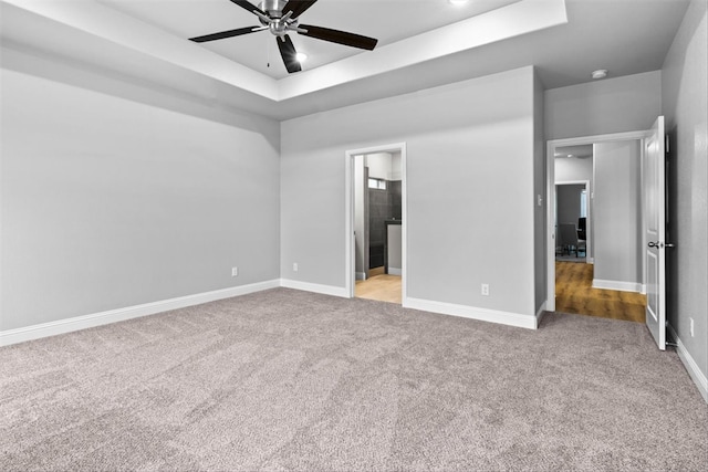 unfurnished bedroom featuring ensuite bathroom, ceiling fan, a raised ceiling, and light carpet