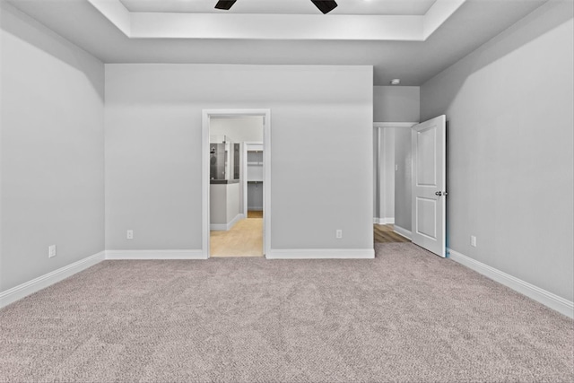 unfurnished bedroom with a walk in closet, light colored carpet, a raised ceiling, and ceiling fan