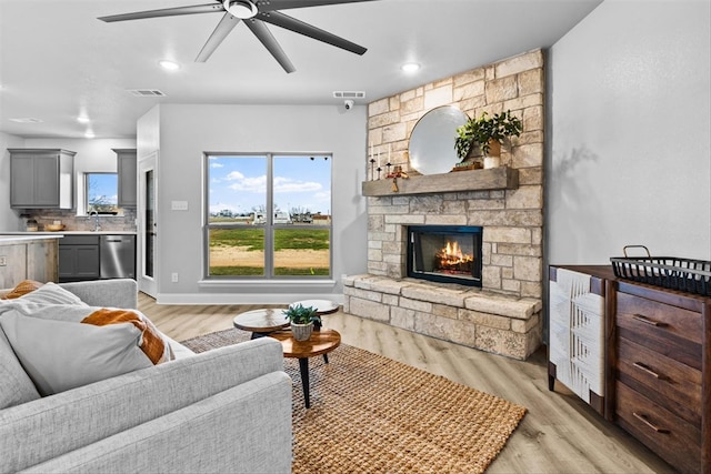 living room with a stone fireplace, ceiling fan, and light hardwood / wood-style flooring