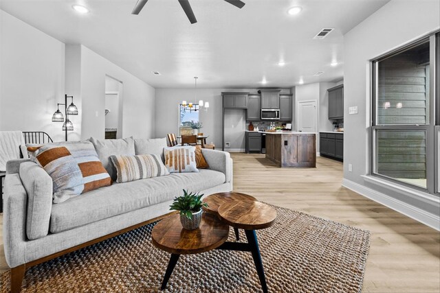 living room featuring ceiling fan with notable chandelier and light hardwood / wood-style flooring