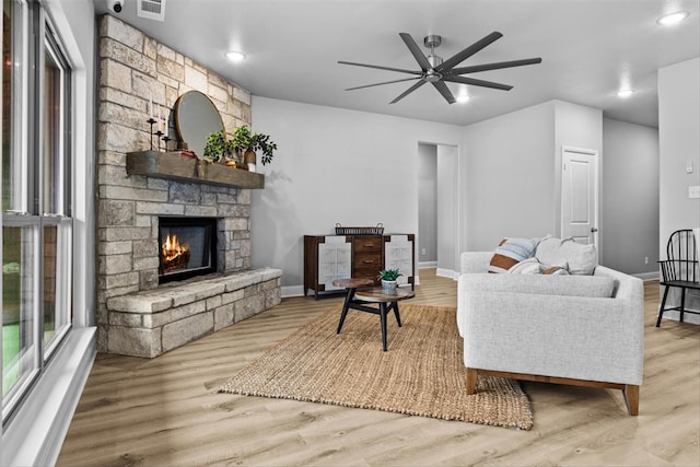 living room featuring ceiling fan, a stone fireplace, and light hardwood / wood-style flooring