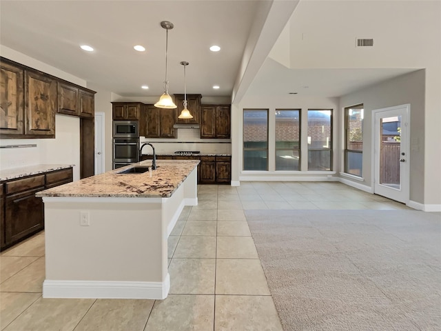 kitchen featuring light stone counters, appliances with stainless steel finishes, decorative light fixtures, and a center island with sink