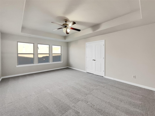 carpeted empty room featuring ceiling fan and a raised ceiling