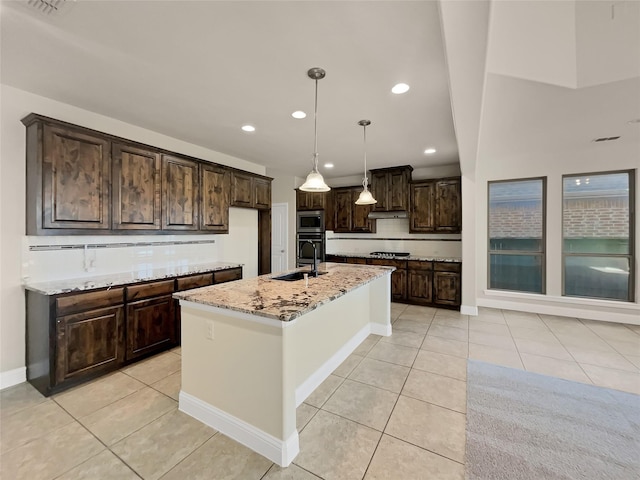 kitchen featuring sink, light stone counters, a center island with sink, appliances with stainless steel finishes, and pendant lighting