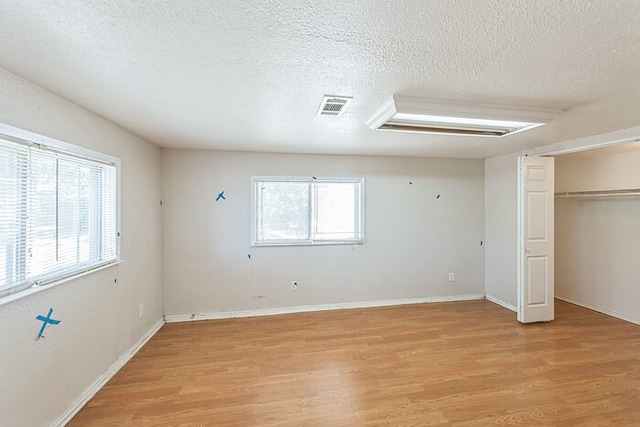 unfurnished bedroom featuring multiple windows, a textured ceiling, and light hardwood / wood-style flooring