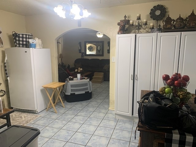 interior space with a notable chandelier, white cabinetry, white refrigerator, and light tile floors