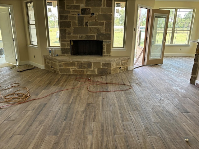 unfurnished living room with baseboards, wood finished floors, and a stone fireplace