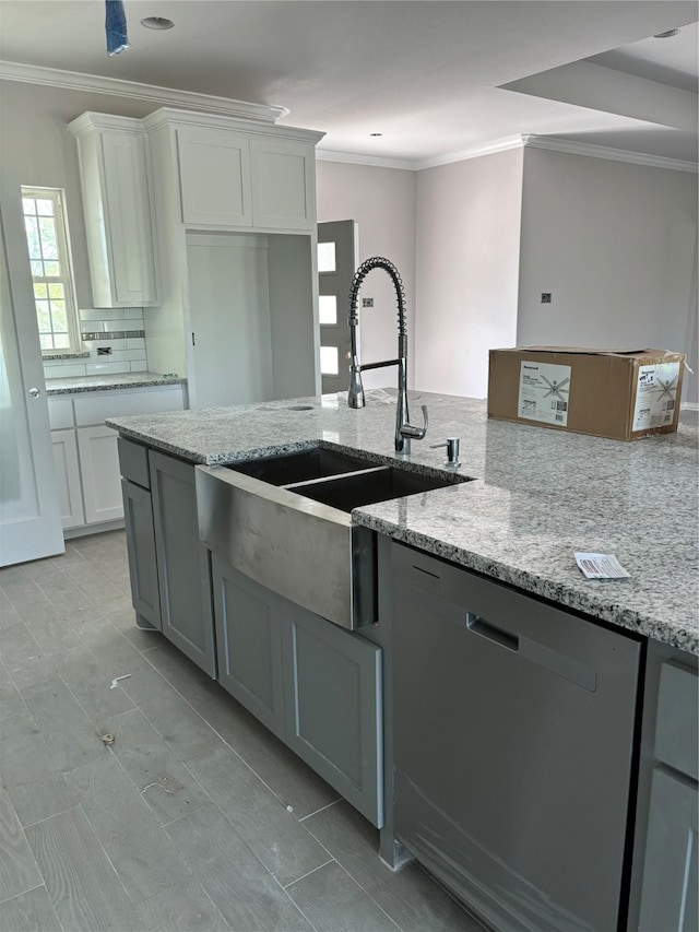 kitchen featuring stainless steel dishwasher, a sink, light stone countertops, and crown molding