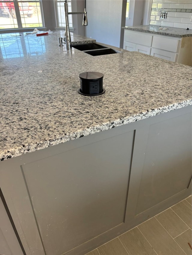 kitchen featuring decorative backsplash, light stone counters, white cabinets, and a sink