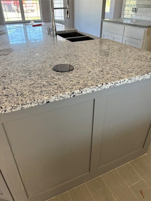 kitchen with decorative backsplash, a sink, white cabinetry, and light stone countertops