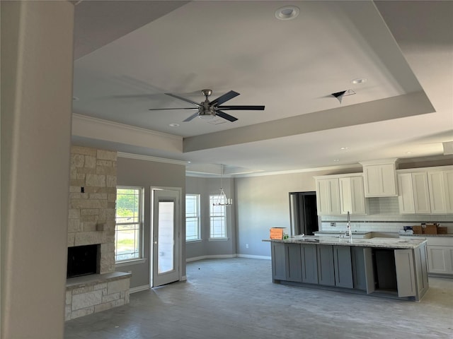 kitchen with ornamental molding, a tray ceiling, a kitchen island with sink, and white cabinets