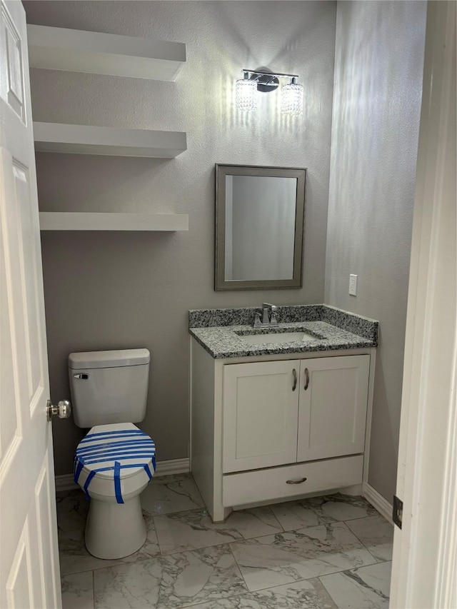 bathroom with toilet, marble finish floor, baseboards, and vanity