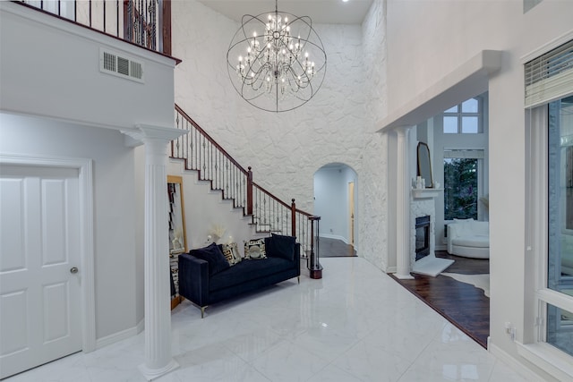 entryway with a chandelier, a high ceiling, ornate columns, wood-type flooring, and a fireplace