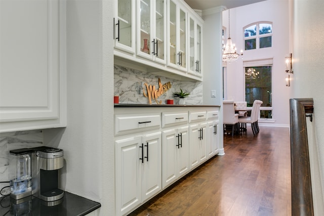 bar with dark hardwood / wood-style flooring, tasteful backsplash, white cabinetry, and a chandelier