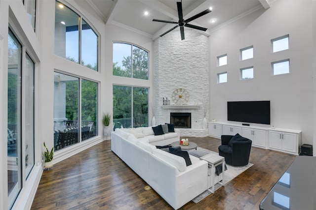 living room with ceiling fan, dark wood-type flooring, crown molding, a stone fireplace, and high vaulted ceiling