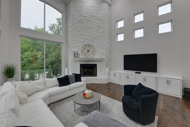 living room featuring dark hardwood / wood-style floors, a stone fireplace, and a high ceiling