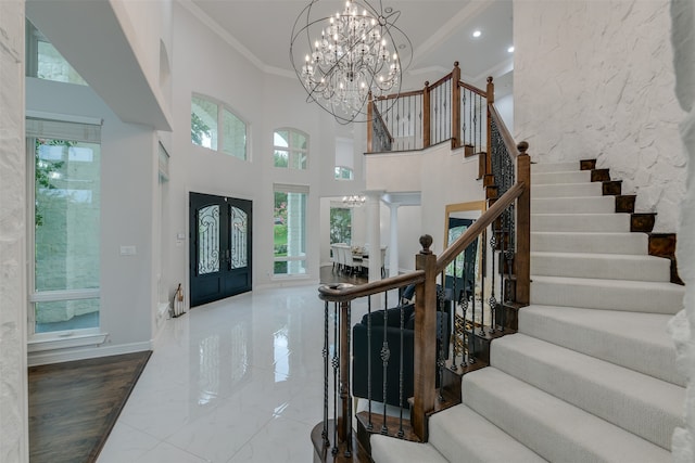 tiled foyer entrance with a notable chandelier, crown molding, and a high ceiling