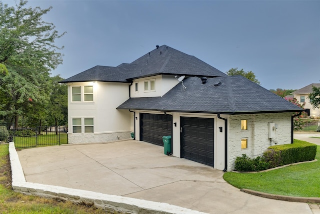 exterior space featuring roof with shingles, stucco siding, fence, stone siding, and driveway