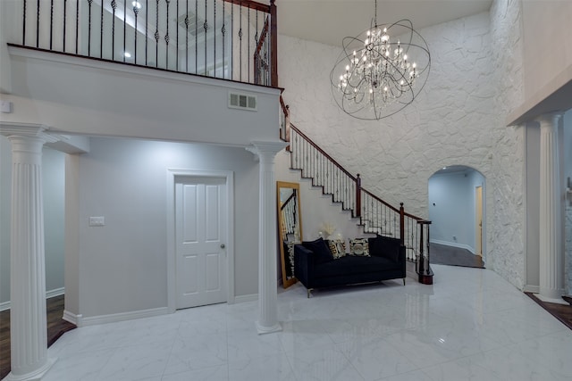 stairs featuring a towering ceiling, an inviting chandelier, decorative columns, and tile patterned floors