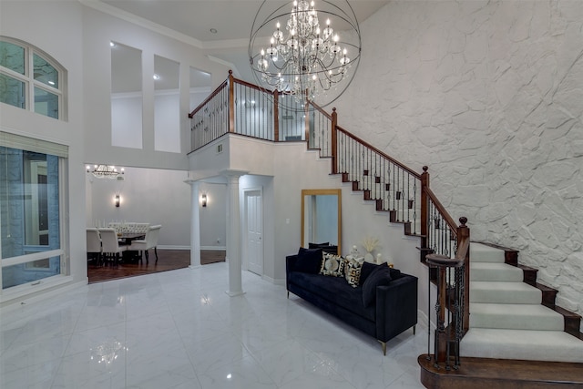 interior space featuring a high ceiling, ornamental molding, wood-type flooring, a chandelier, and decorative columns